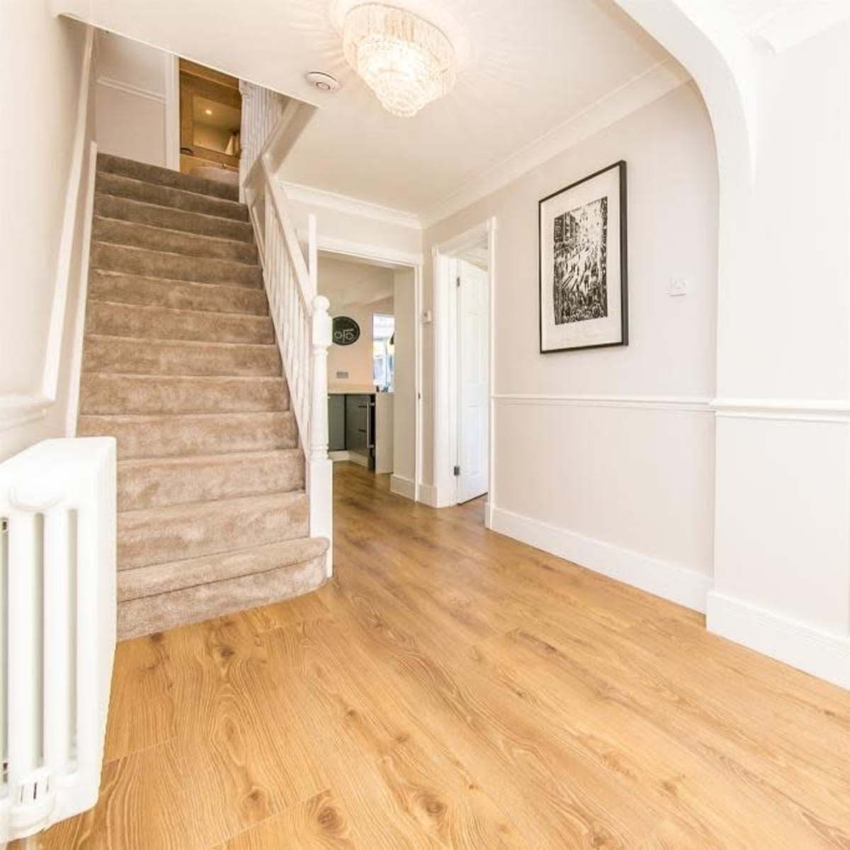 A bright hallway featuring a staircase on the left, a decorative side table on the right, and light-colored walls.
