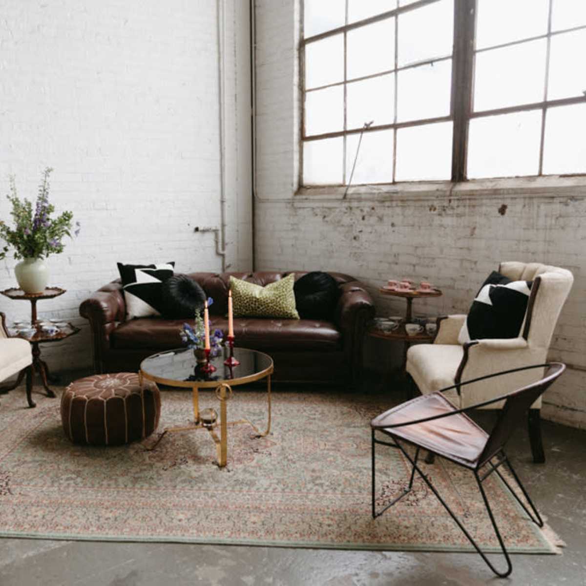 A cozy living room with a brown leather sofa, two upholstered armchairs, a round coffee table, and a patterned rug, all arranged near a large window.