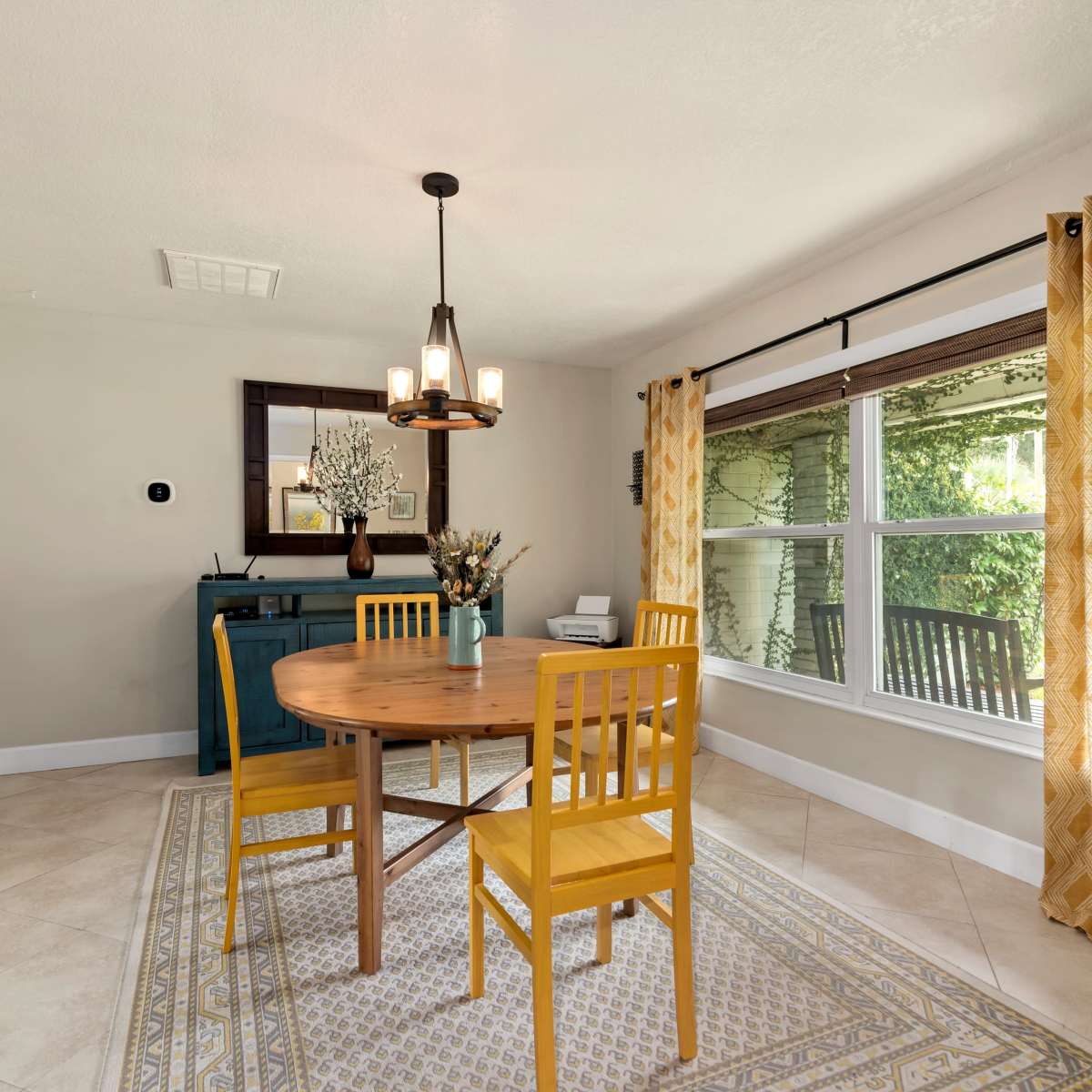 The dining area features a round wooden table with four yellow chairs, surrounded by windows that let in natural light.