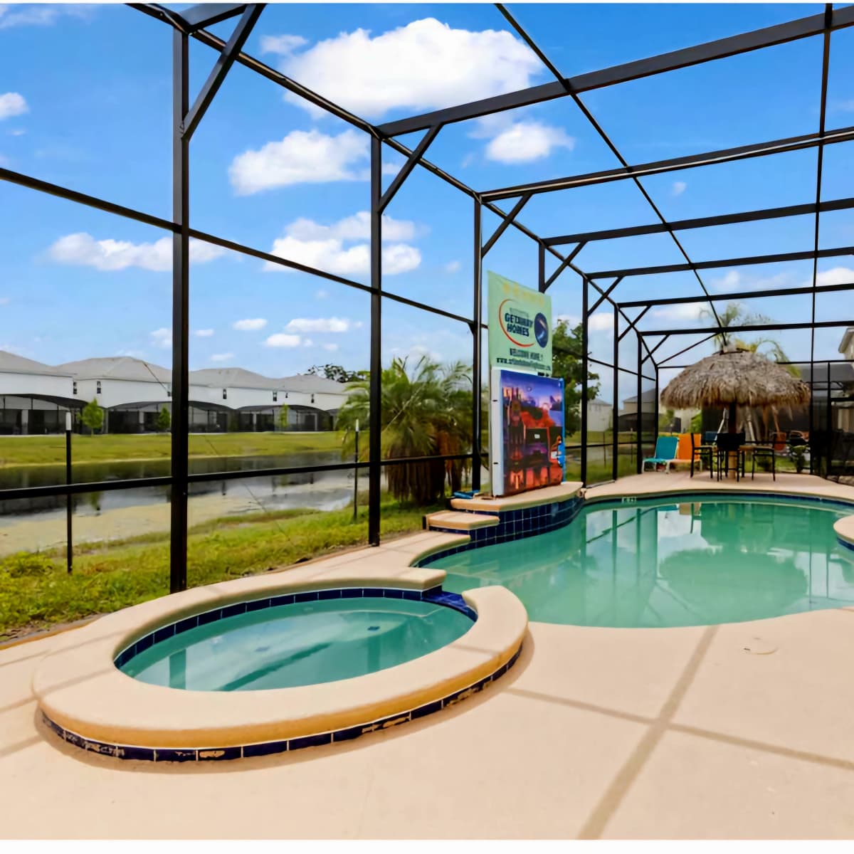 A screened-in patio featuring a swimming pool, a spa, and a thatched umbrella, with residential homes visible in the background.