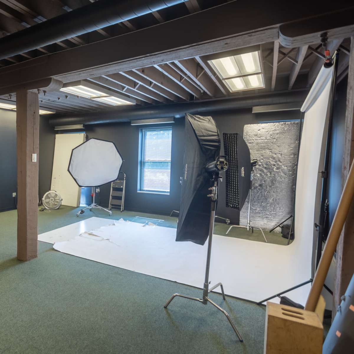 A photography studio with a partially set-up backdrop, a large softbox, and various lighting equipment arranged in a spacious room.