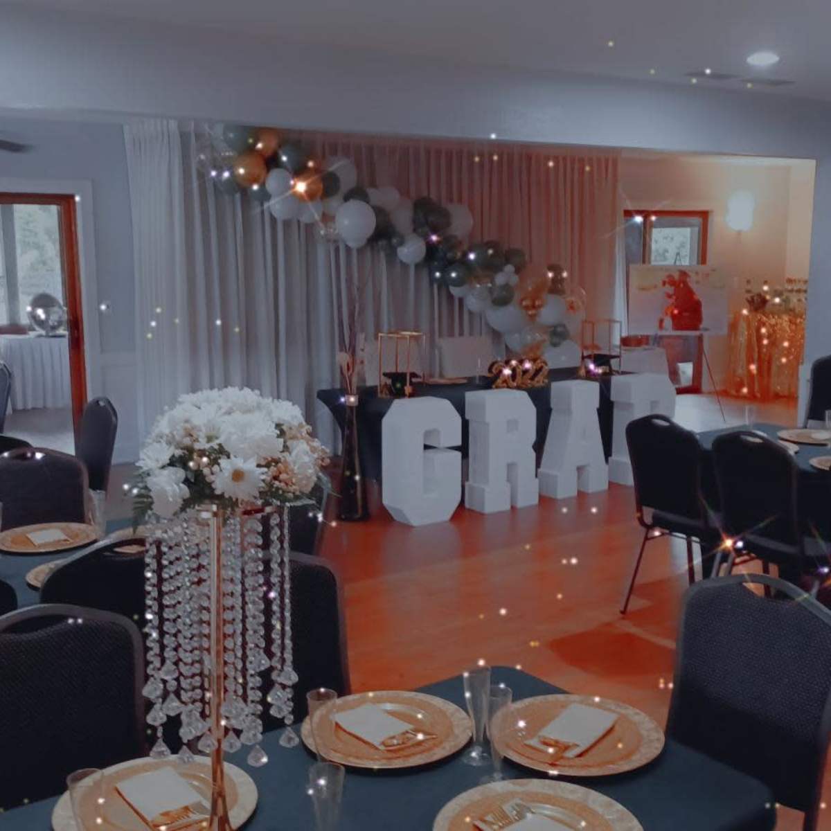 A banquet hall set up for a celebration, featuring tables with black cloths, centerpieces, and large decorative letters that spell "GRAD."