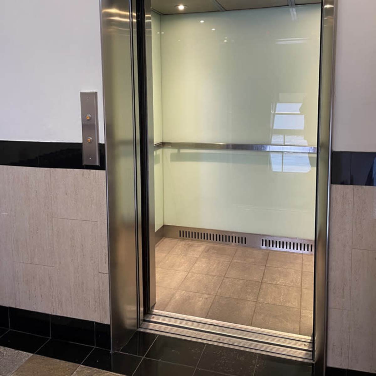 An open elevator with a glass door and tiled flooring in a modern building.