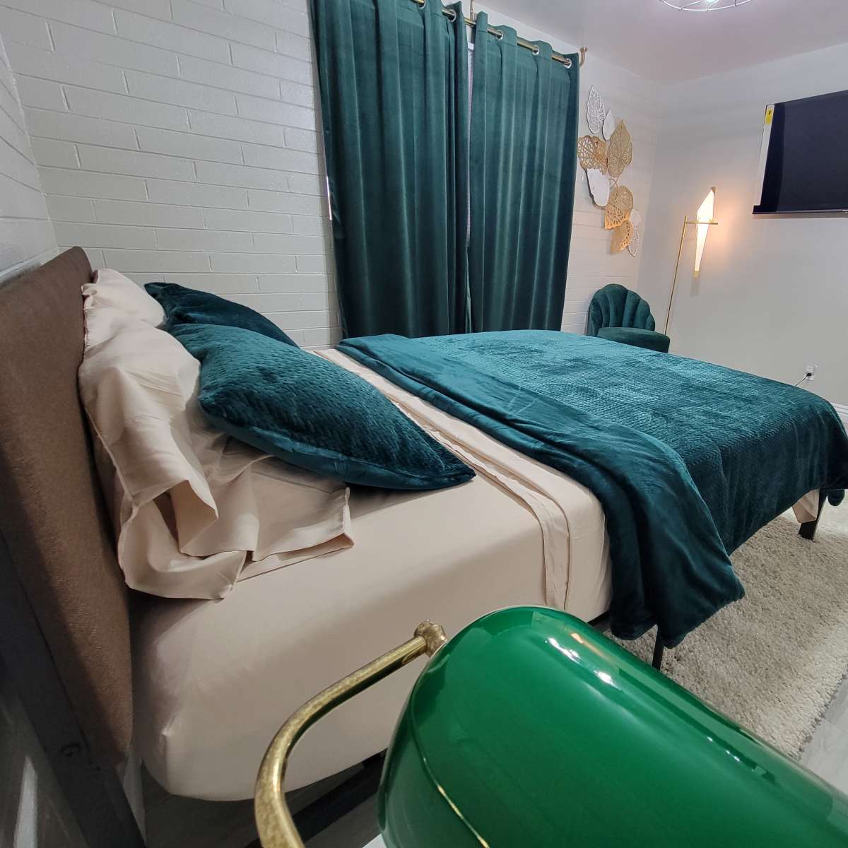 A neatly arranged bedroom featuring a green bedspread, matching curtains, and a wall-mounted television.