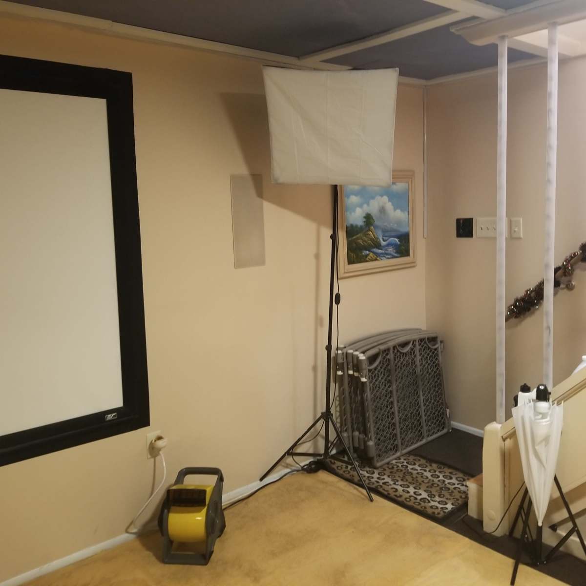 A basement room with a large white screen on one wall, a lighting setup on a tripod, and a staircase leading up.