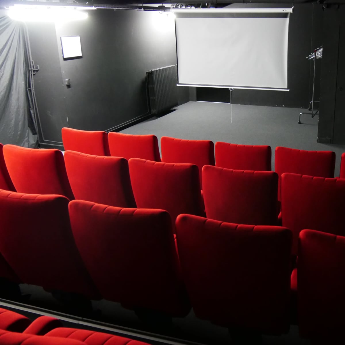 A small theater space with red seating facing a blank projection screen.