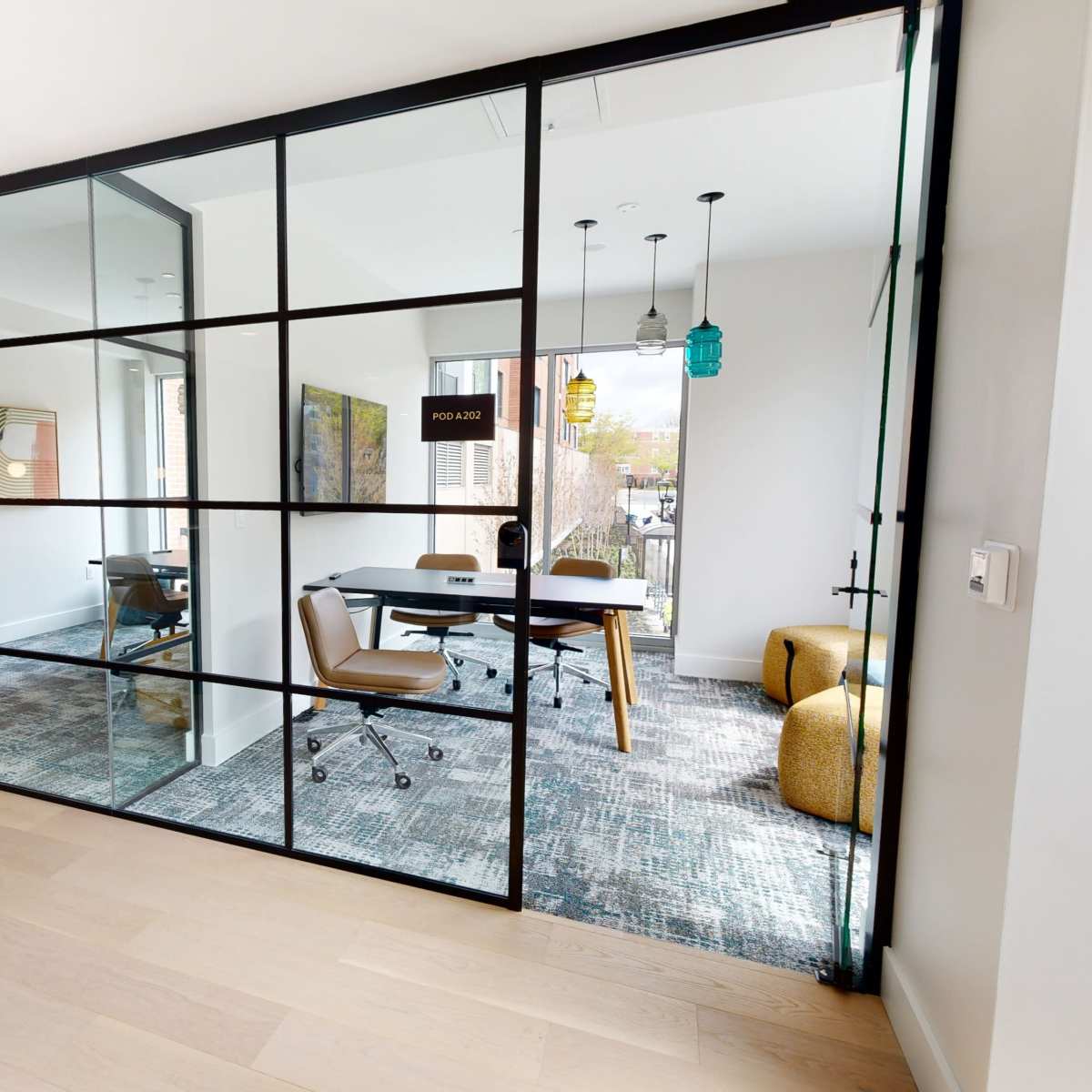 A modern office space is divided by glass walls, featuring a meeting area with a conference table and chairs, and accented by green plants outside.