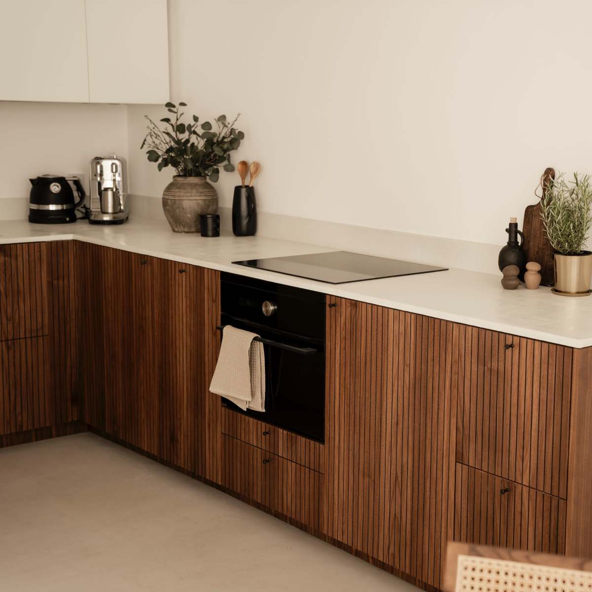 A modern kitchen features a minimalist design with wood cabinetry, a black oven, and a few decorative plants on the counter.