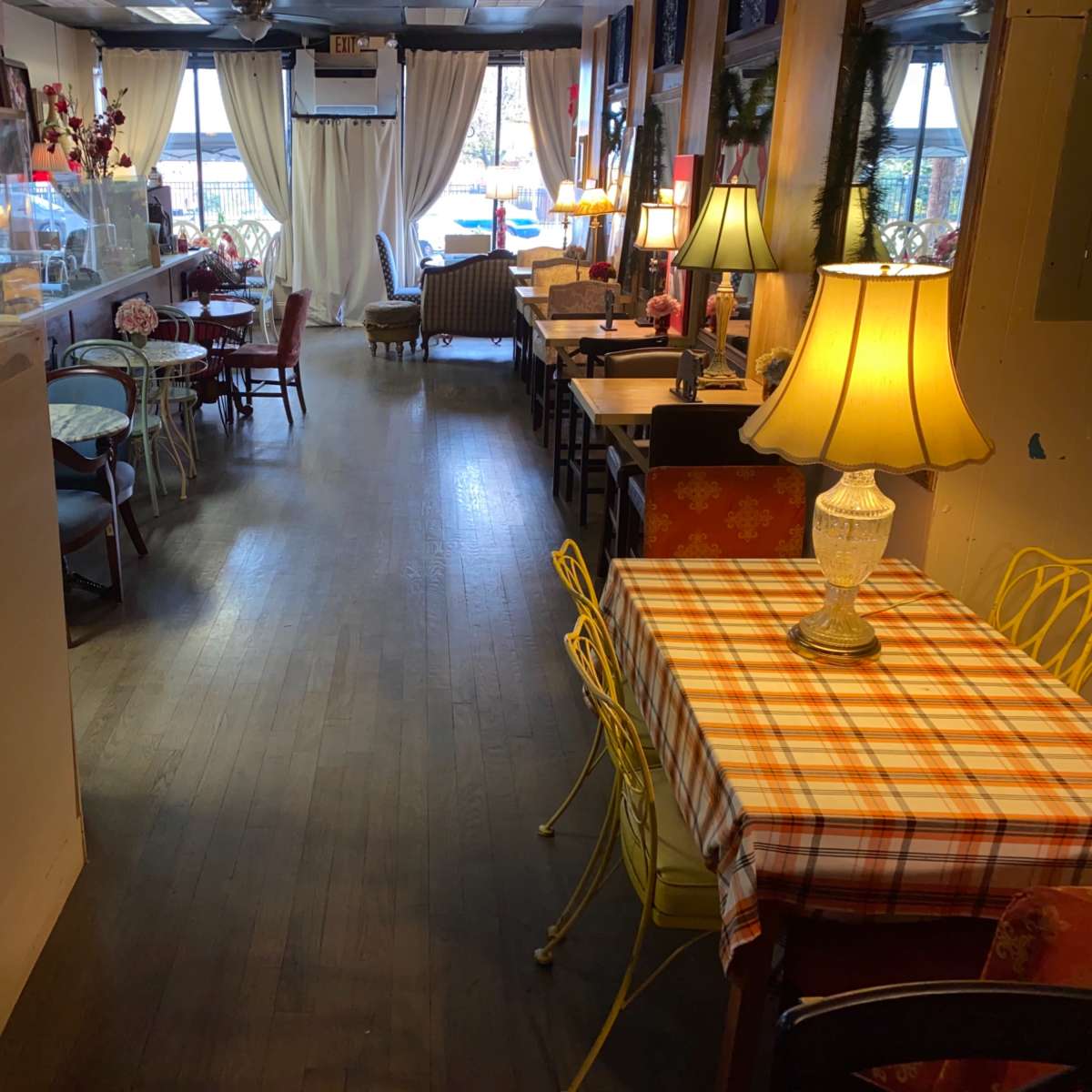 A cozy café interior with wooden flooring, tables of varying styles, and soft lighting from lamps placed around the space.