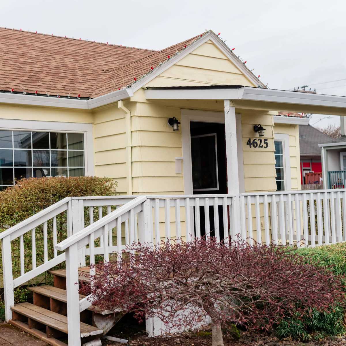 A single-story yellow house with a front porch, a sloped roof, and neatly trimmed landscaping.