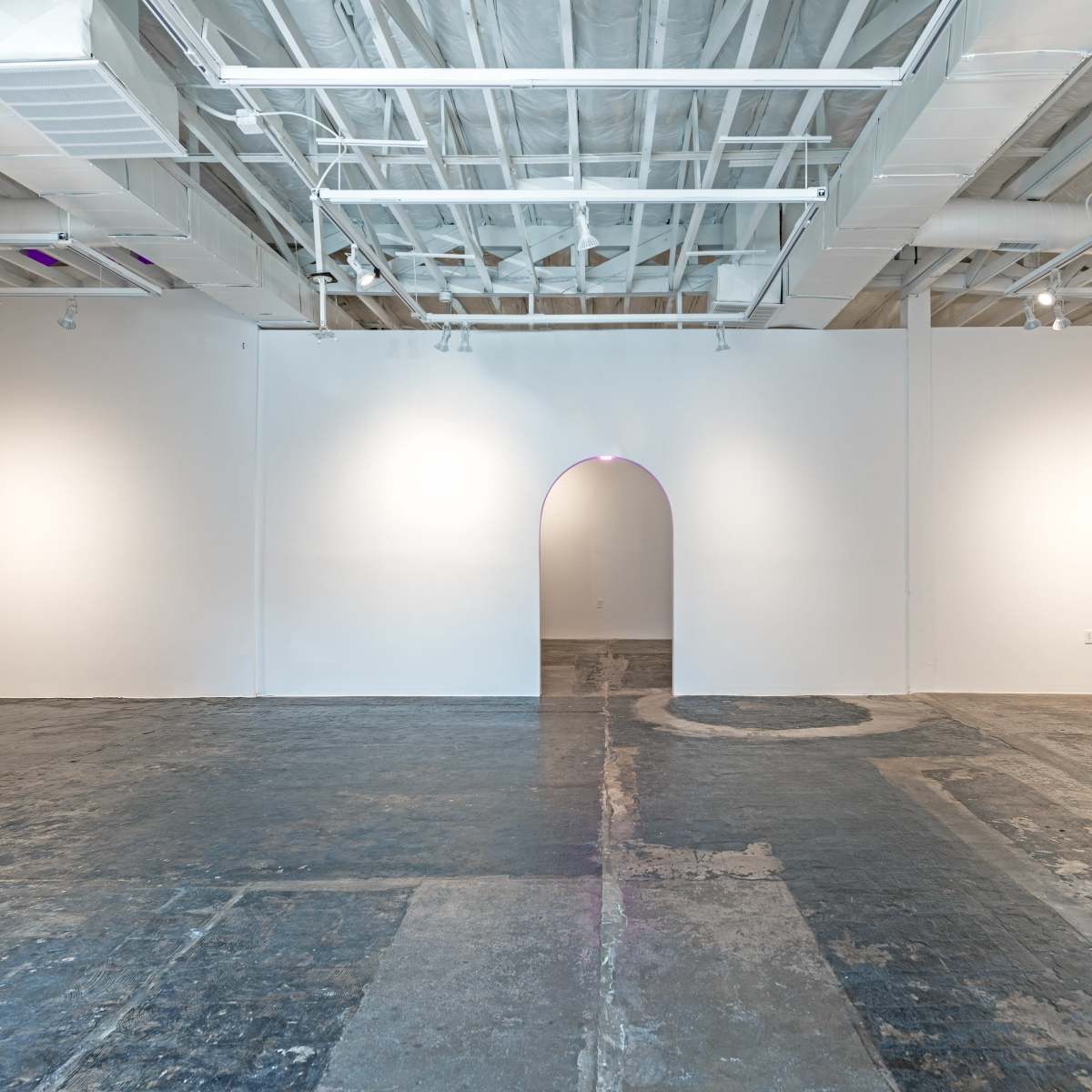 A spacious, empty art gallery with white walls and a curved archway leading to a darker area.