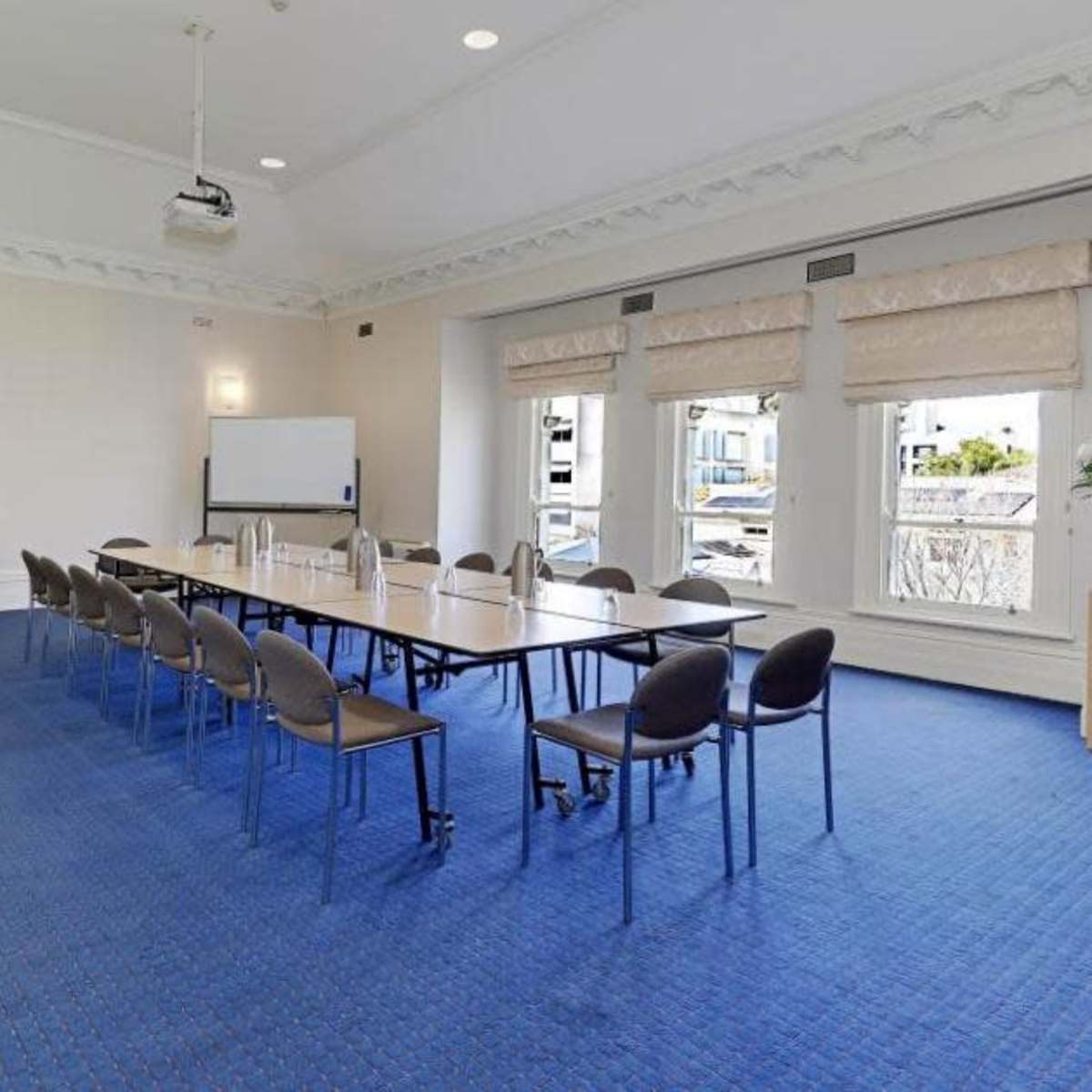 A meeting room features a long table with chairs, large windows, and a projector mounted on the ceiling.