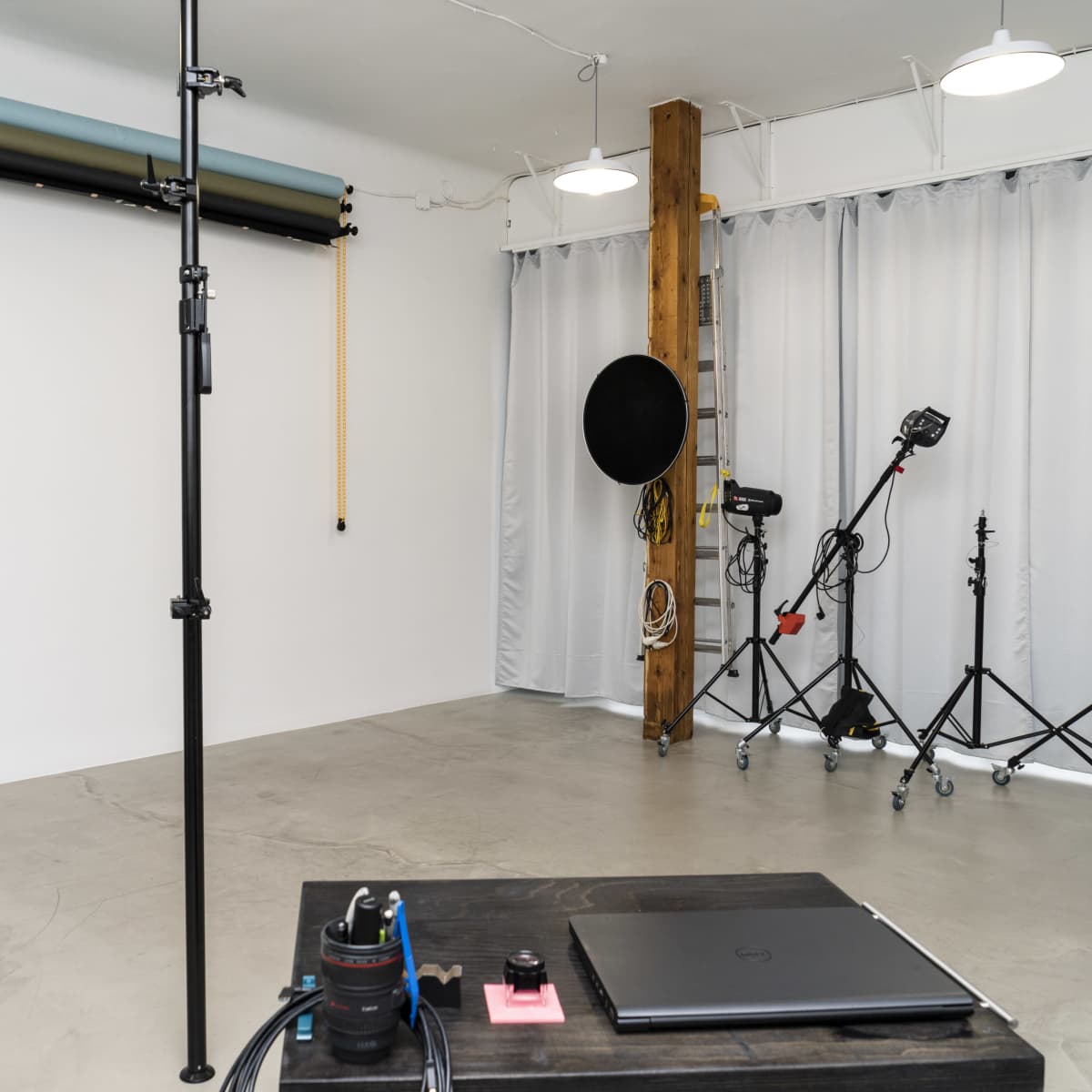 A spacious studio with a minimalist design, featuring a large empty wall, photography equipment, and a laptop on a table.
