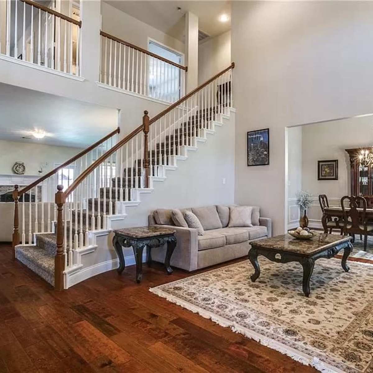 A spacious living room with a staircase, hardwood floors, and a dining area in an adjacent open layout.