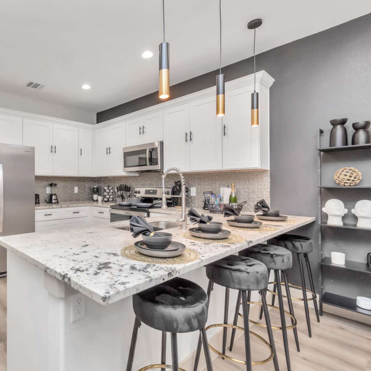 A modern kitchen features white cabinetry, stainless steel appliances, and a marble-topped island with black bar stools.