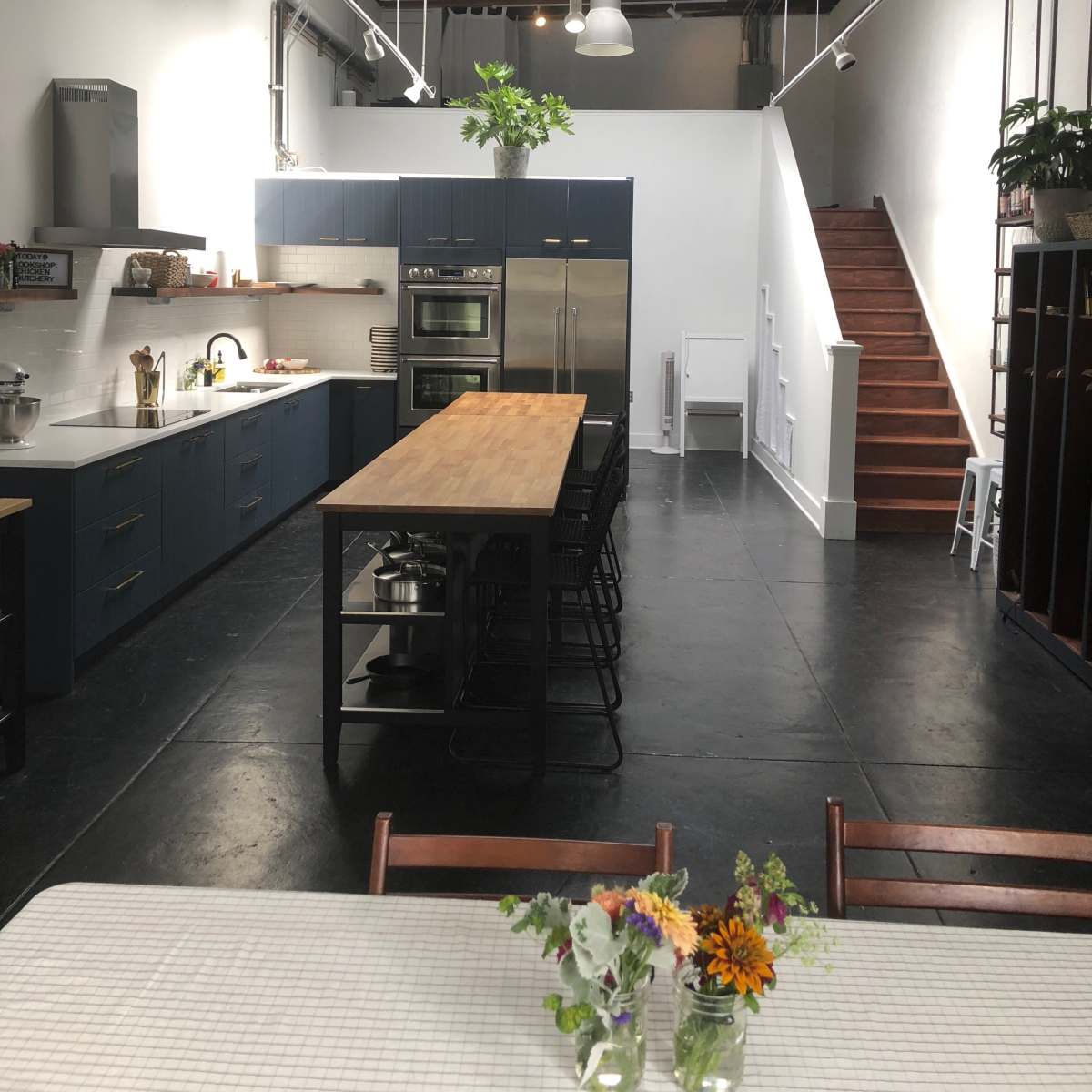 A spacious modern kitchen with a large wooden island, stainless steel appliances, and a staircase leading to an upper level.