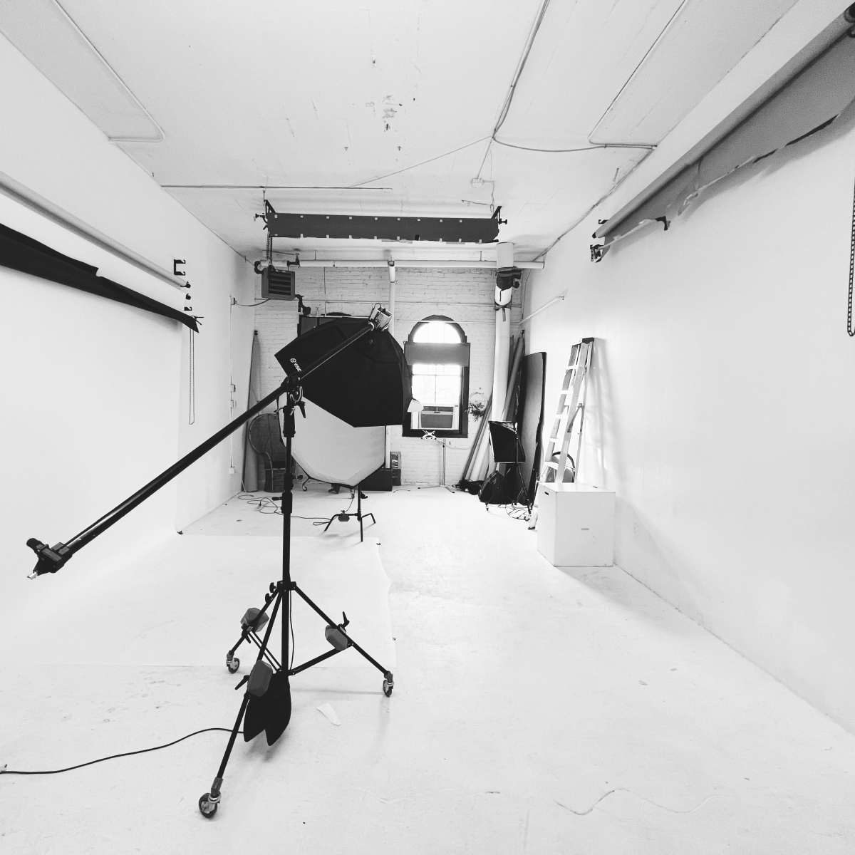 A photography studio with a white backdrop, lighting equipment, and a ladder against the wall.