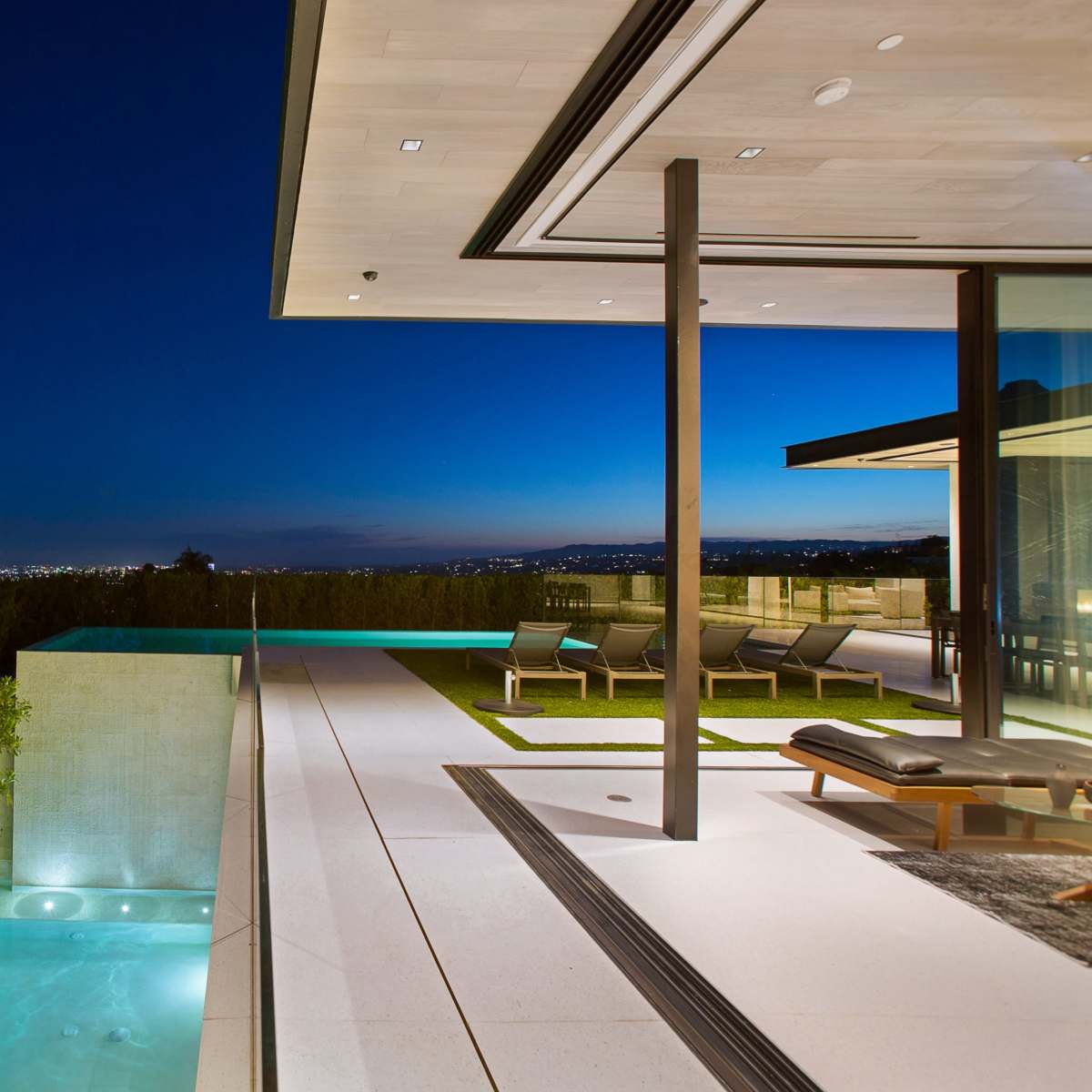 This image shows a modern villa with a swimming pool and a view of the city skyline at night.