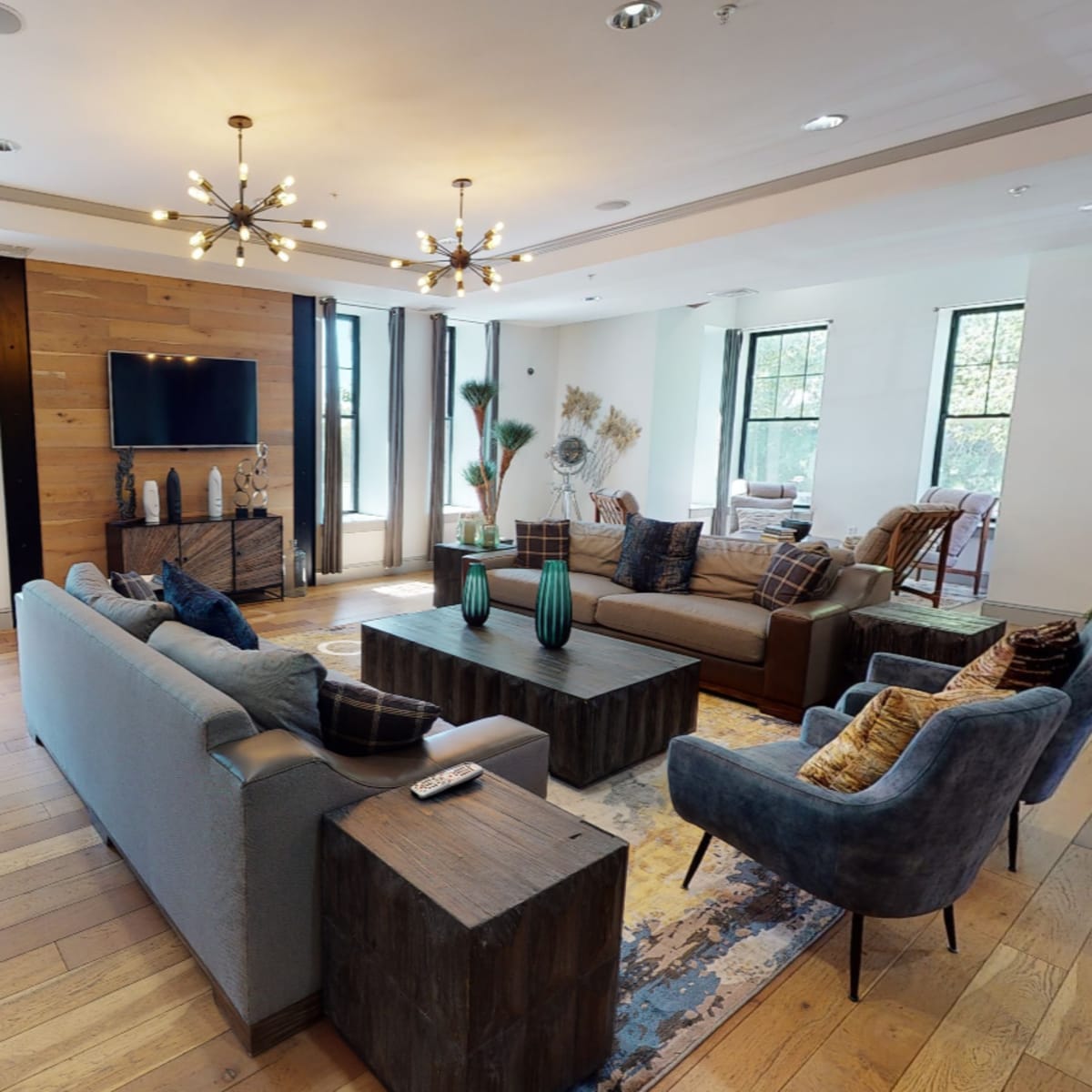 A modern living room features a large coffee table, comfortable seating areas, and windows with natural light.