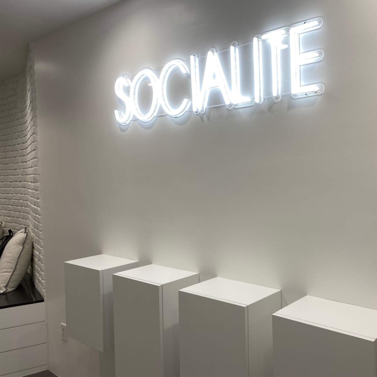 A white wall with the word "SOCIALITE" in illuminated neon letters, above four white pedestals.