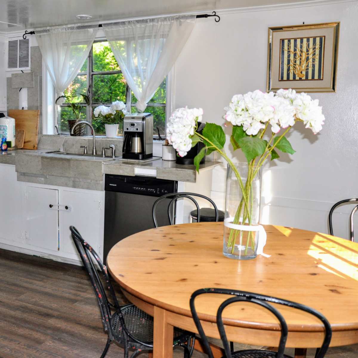 A clean kitchen features white cabinets, a wooden dining table, and a window with a view of the outdoors.