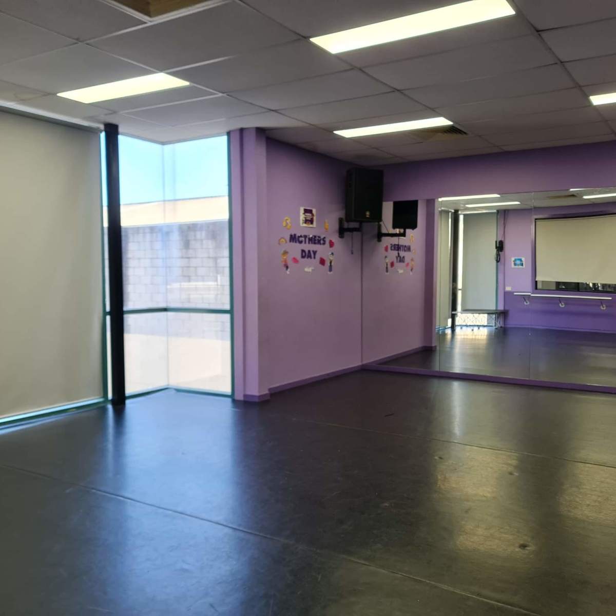 The interior of a purple-walled studio features a large mirror on one side and a window letting in natural light.
