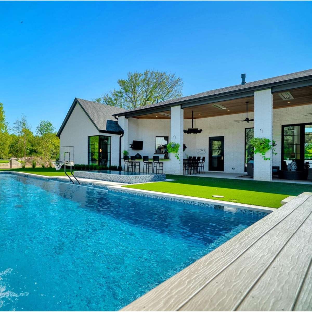 A modern home with a swimming pool in the foreground, featuring a waterfall feature, surrounded by landscaped greenery.