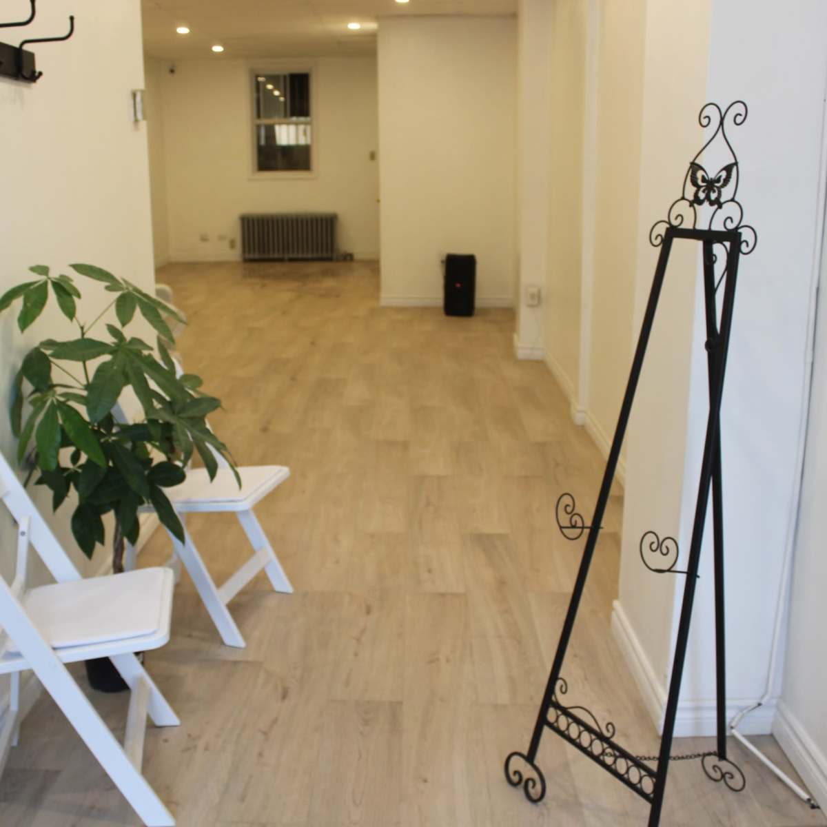 A narrow hallway featuring two white folding chairs, a potted plant, and a decorative metal stand against the wall.