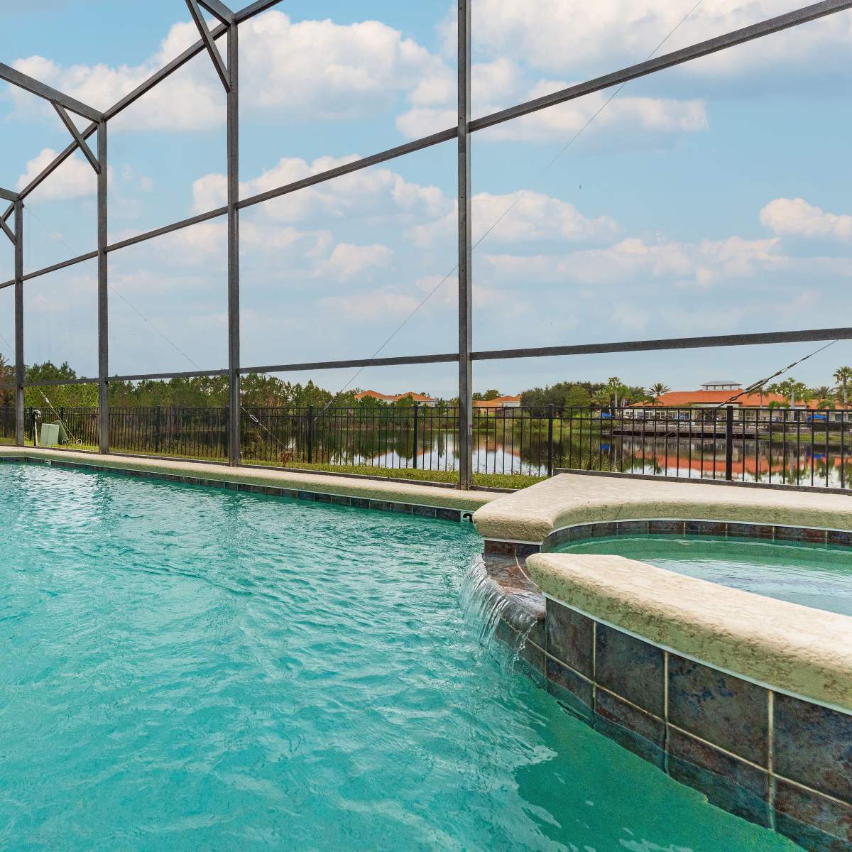 A swimming pool surrounded by a screen enclosure, featuring a spa and views of nearby homes and greenery.