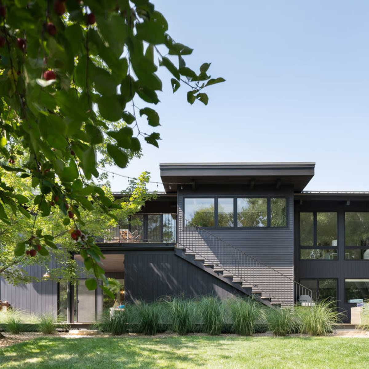 A modern two-story house features large windows and a sleek design, surrounded by greenery and grass.