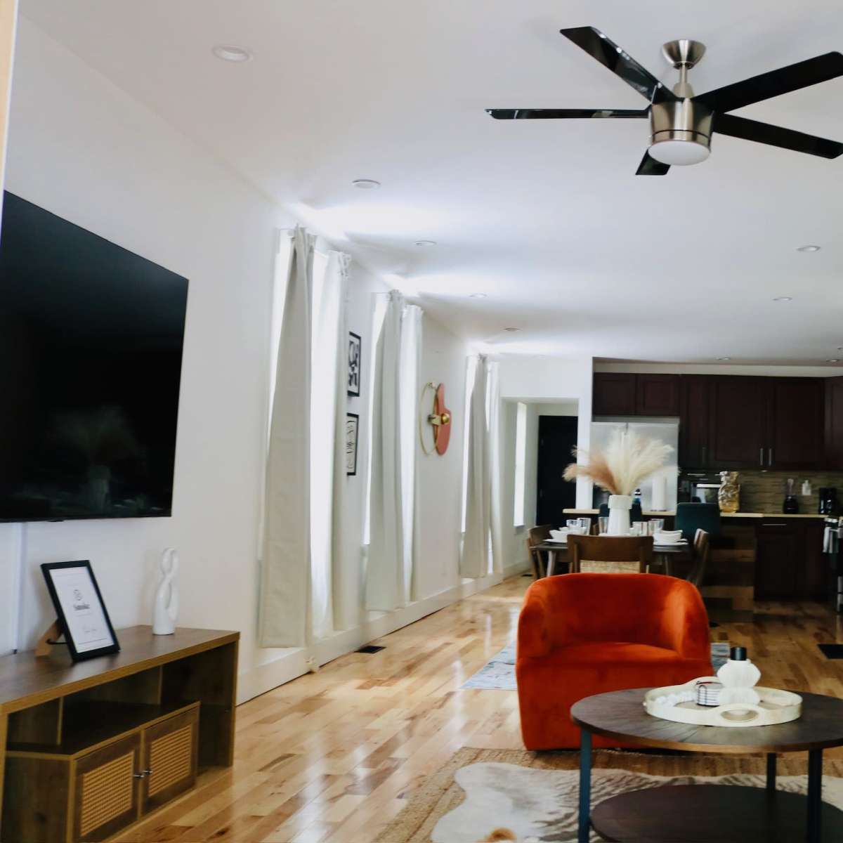 A modern living room with a staircase, featuring a kitchen in the background, a round coffee table, an orange armchair, and a green sofa.
