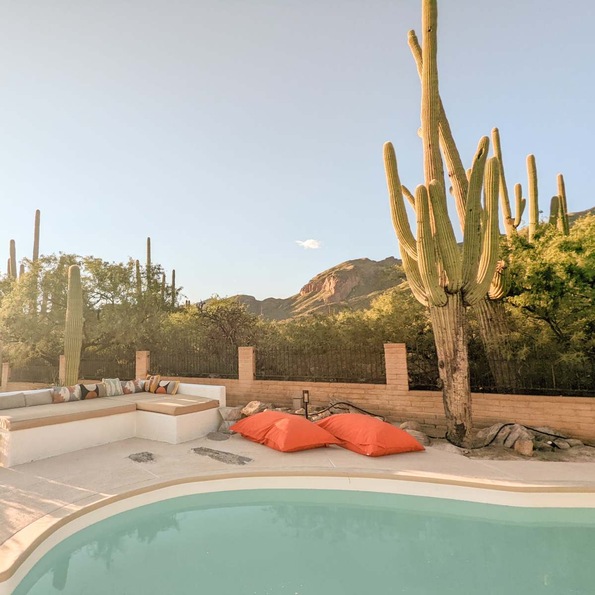 The scene features a swimming pool surrounded by a patio with orange bean bag chairs and cacti against a mountainous backdrop.