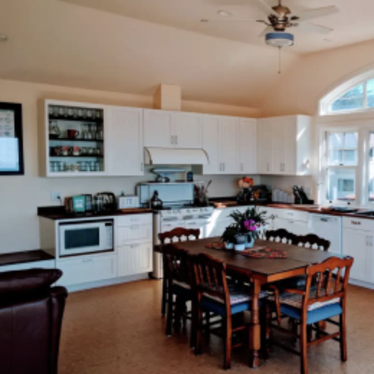 A spacious kitchen with white cabinetry, a large table surrounded by chairs, and a window that lets in natural light.