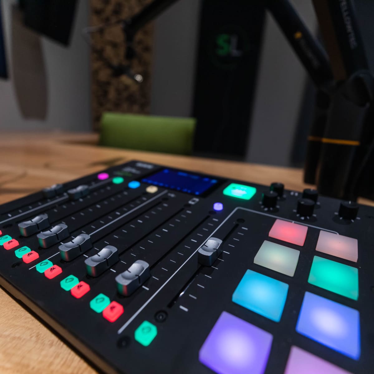 A close-up of a digital audio mixing console with colorful buttons and sliders on a wooden table.