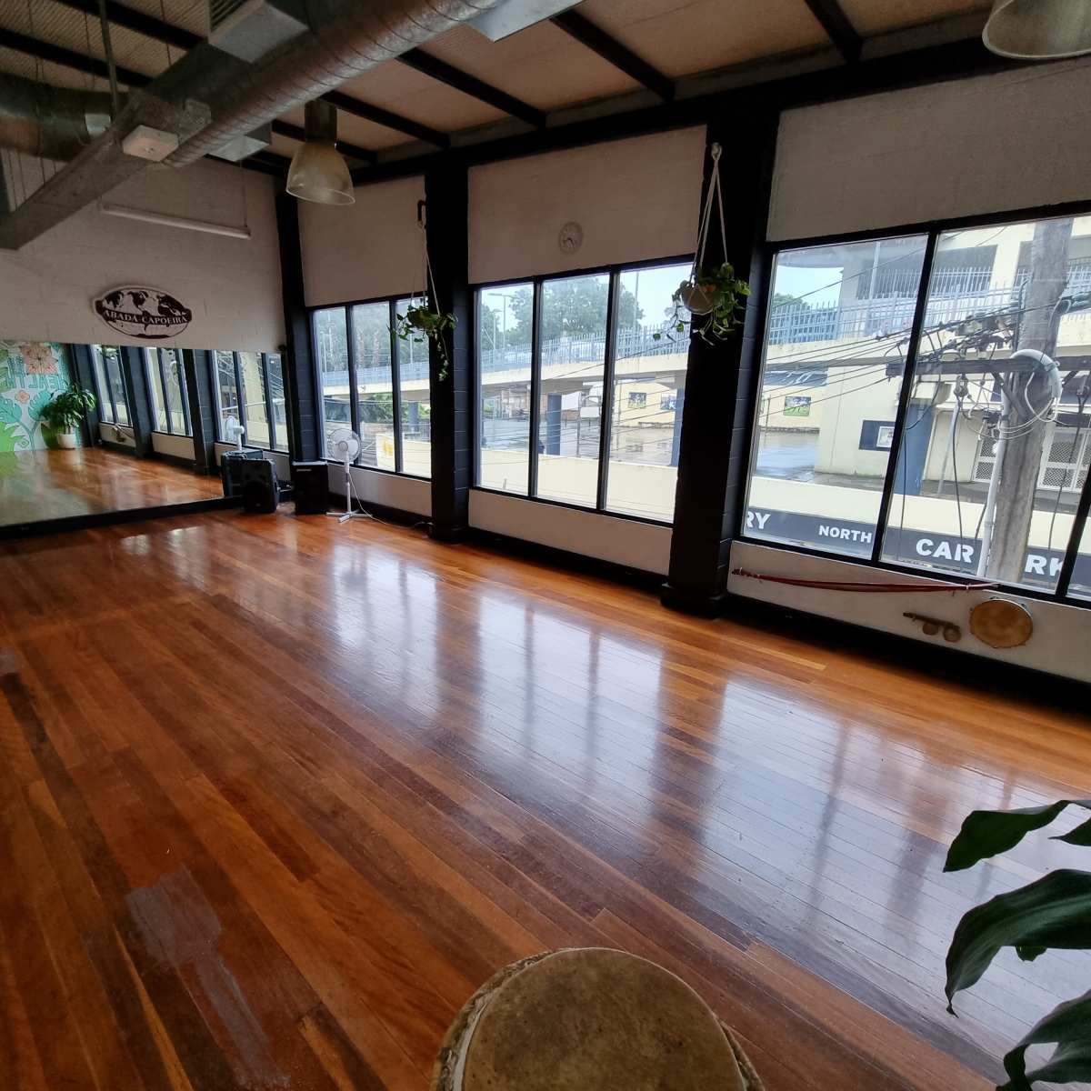 A spacious fitness studio with wooden floors and large windows, providing a view of the outside.