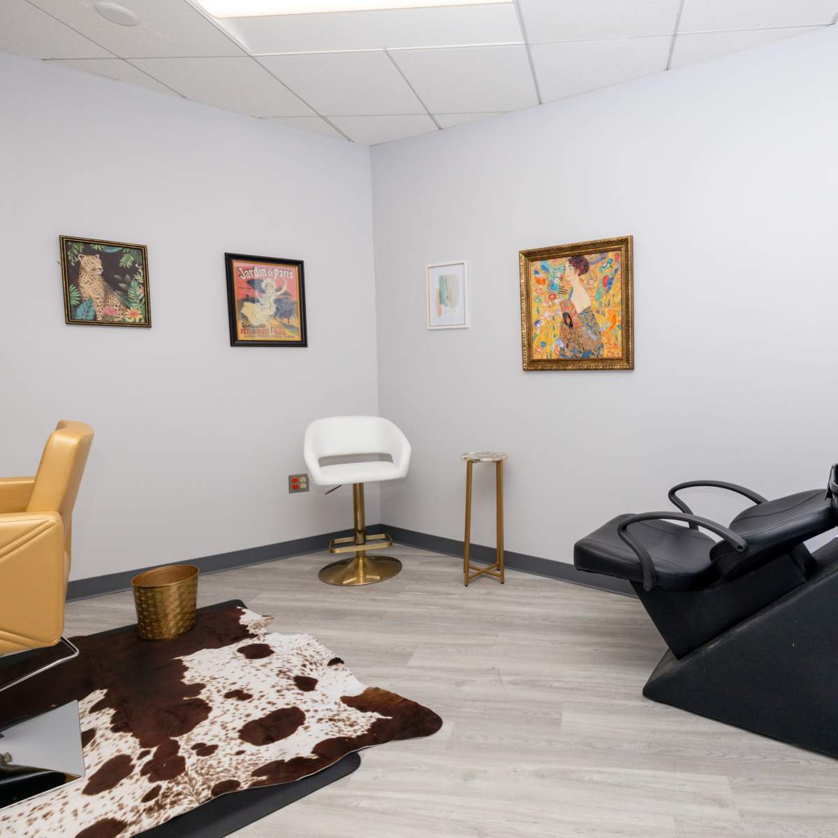 A modern hair salon interior featuring a styling chair, a shampoo station, and framed artwork on the walls.