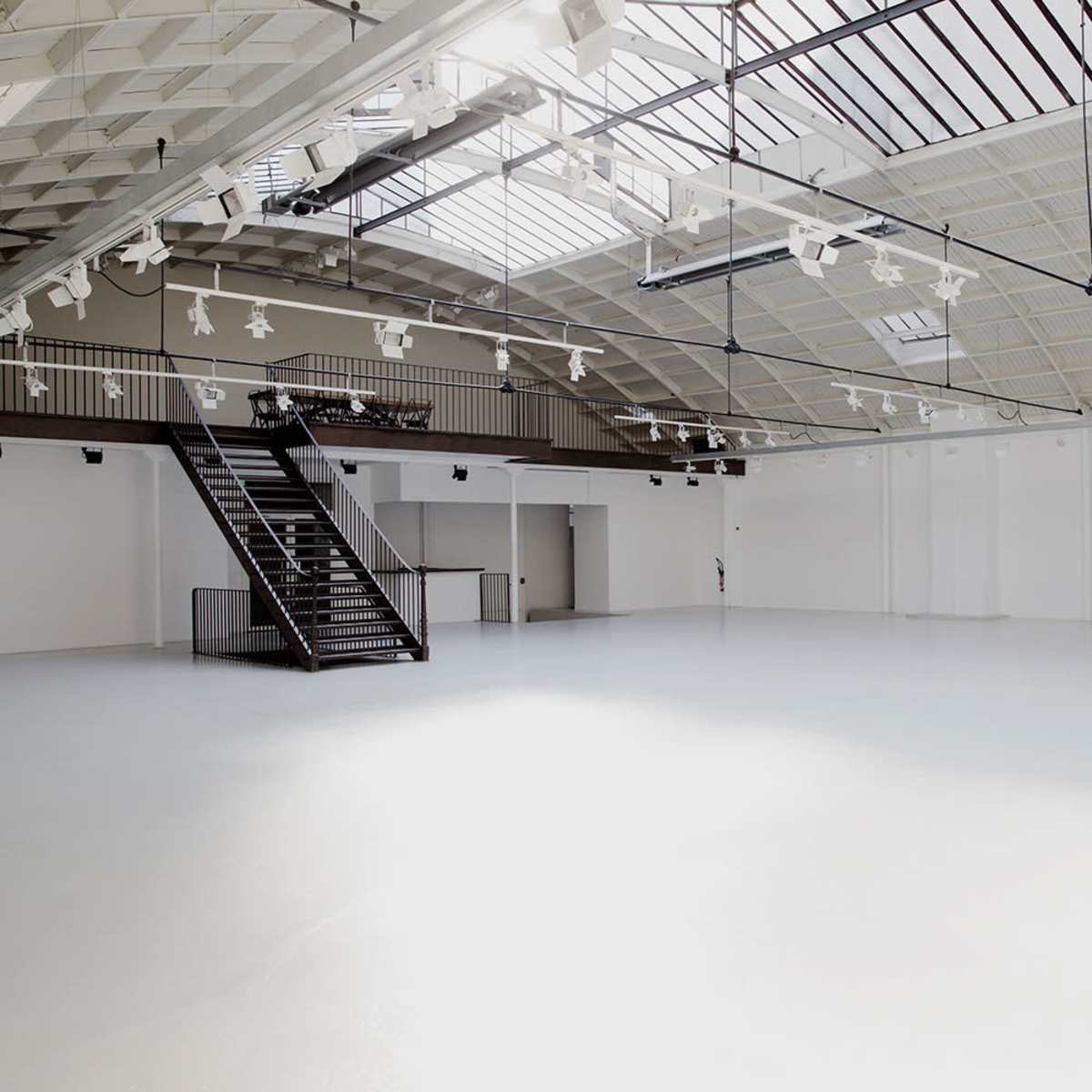 A spacious, empty room with a high ceiling, large skylights, and a staircase on one side.