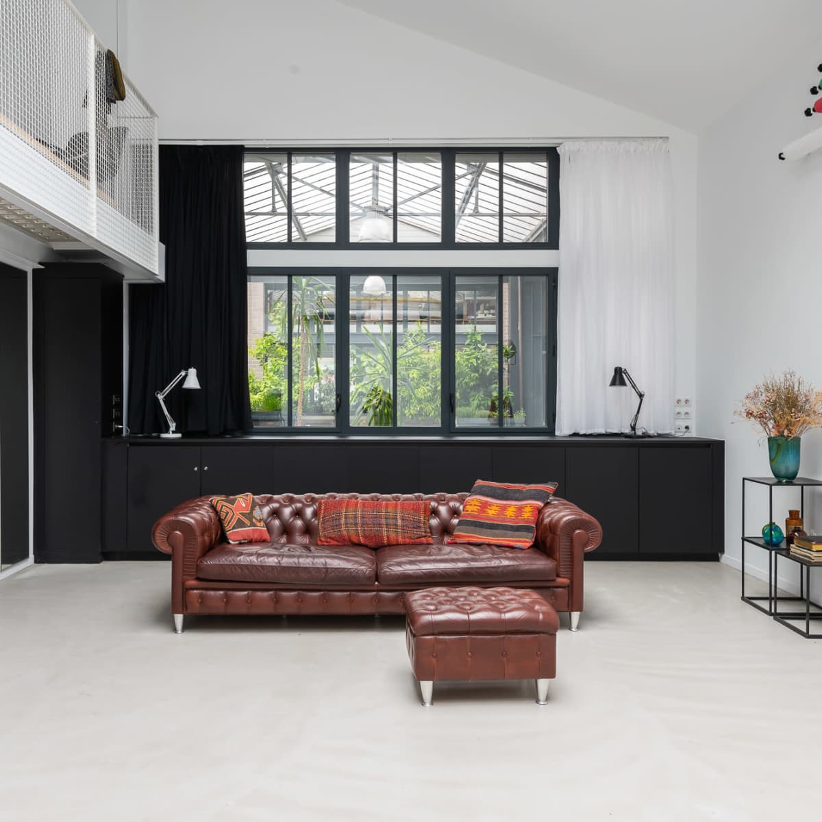 A spacious interior with a leather chesterfield sofa, a coffee table, and large windows overlooking greenery.