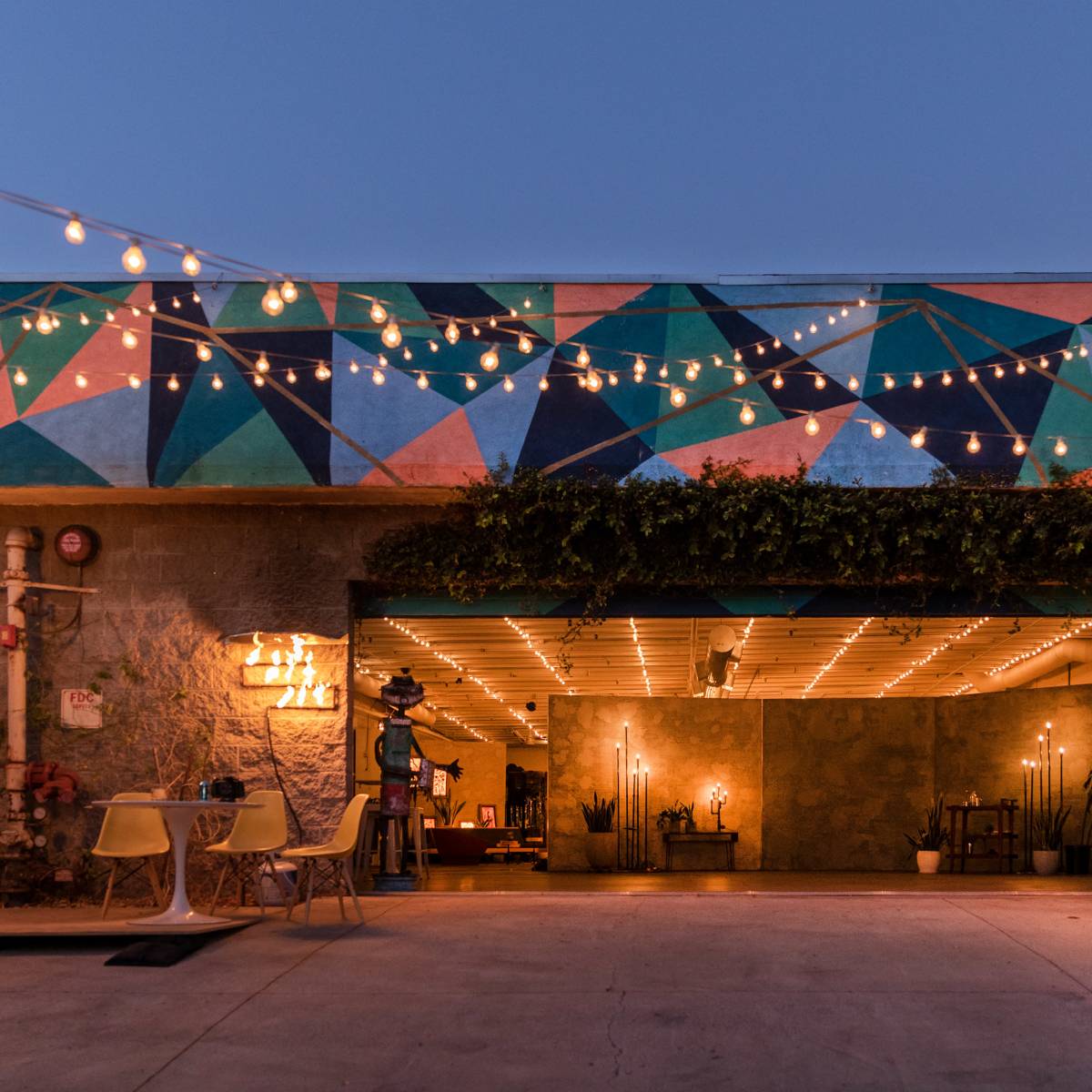 A modern building with a colorful geometric mural and string lights, featuring an open garage space with shelves and decor inside.
