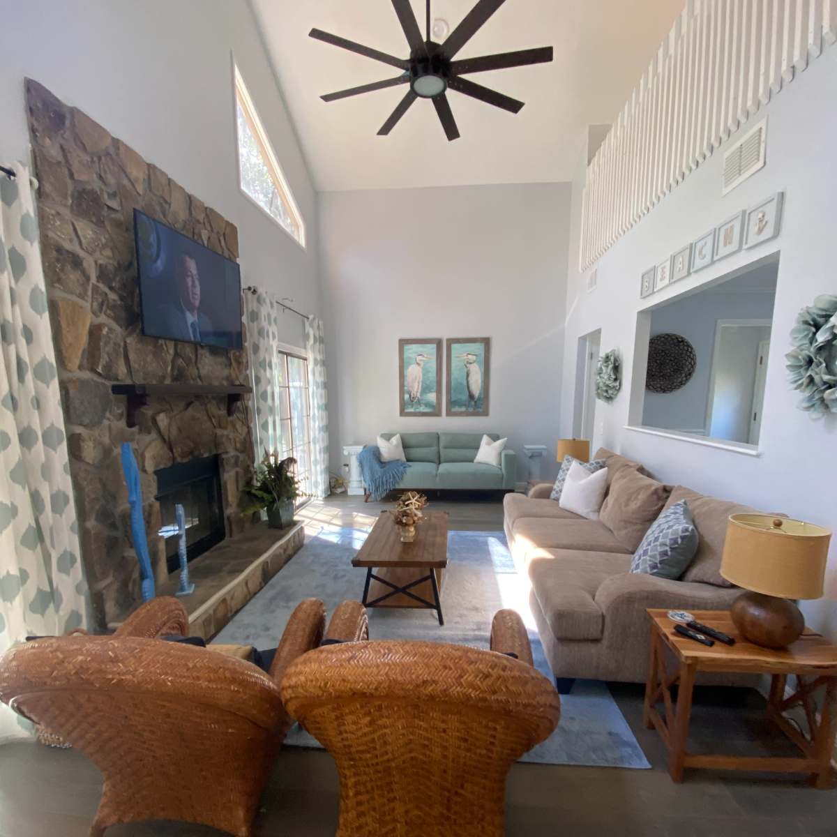 A bright living room with a stone fireplace, a large television on the wall, and a comfortable seating arrangement including a sofa and two chairs.