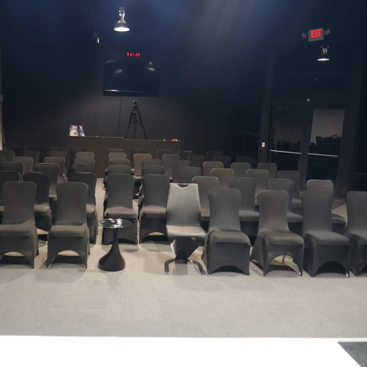 A conference room with neatly arranged black chairs facing a stage and a large screen at the front.