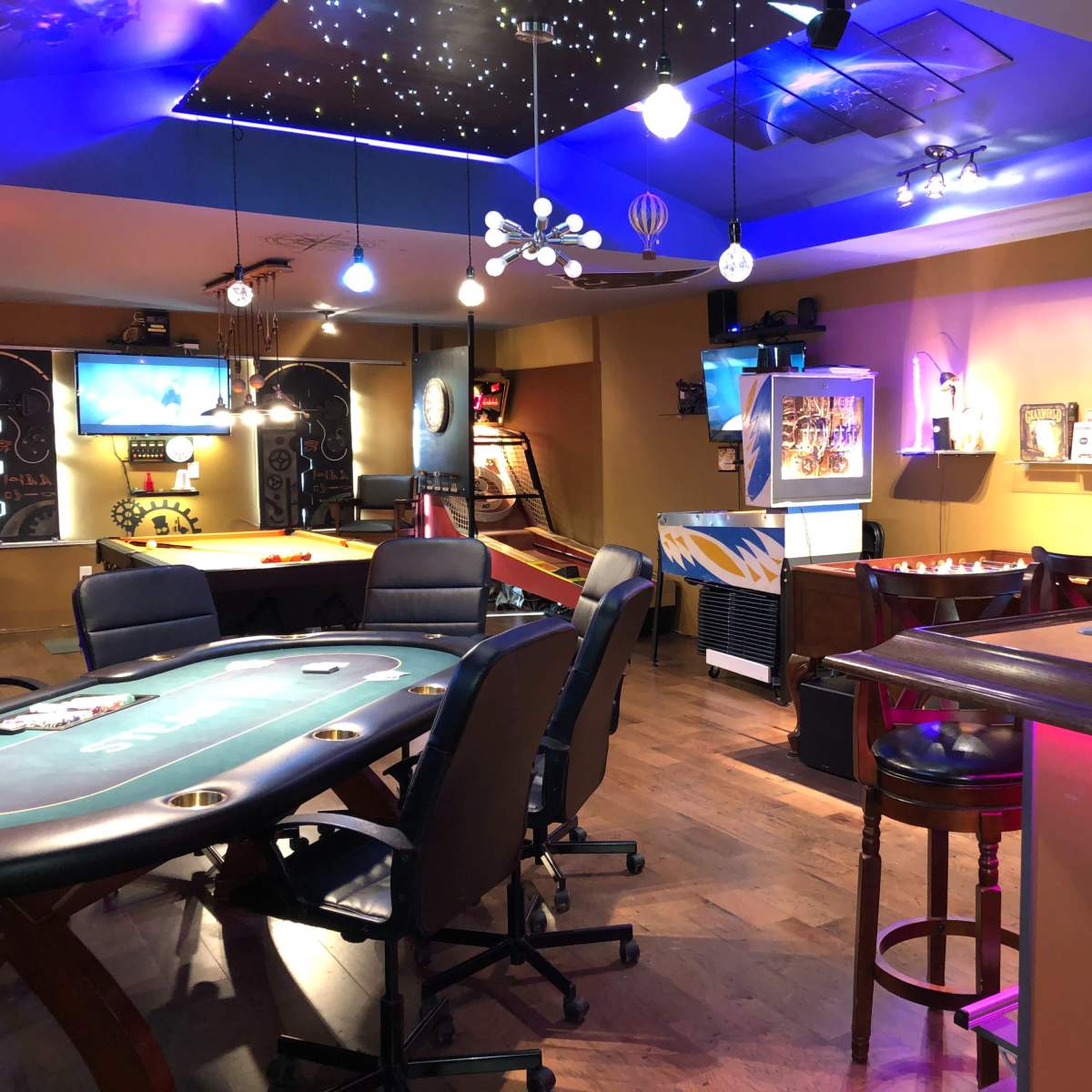 A vibrant gaming and entertainment area featuring a poker table, arcade machine, bar setup, and various seating arrangements under colorful lighting.