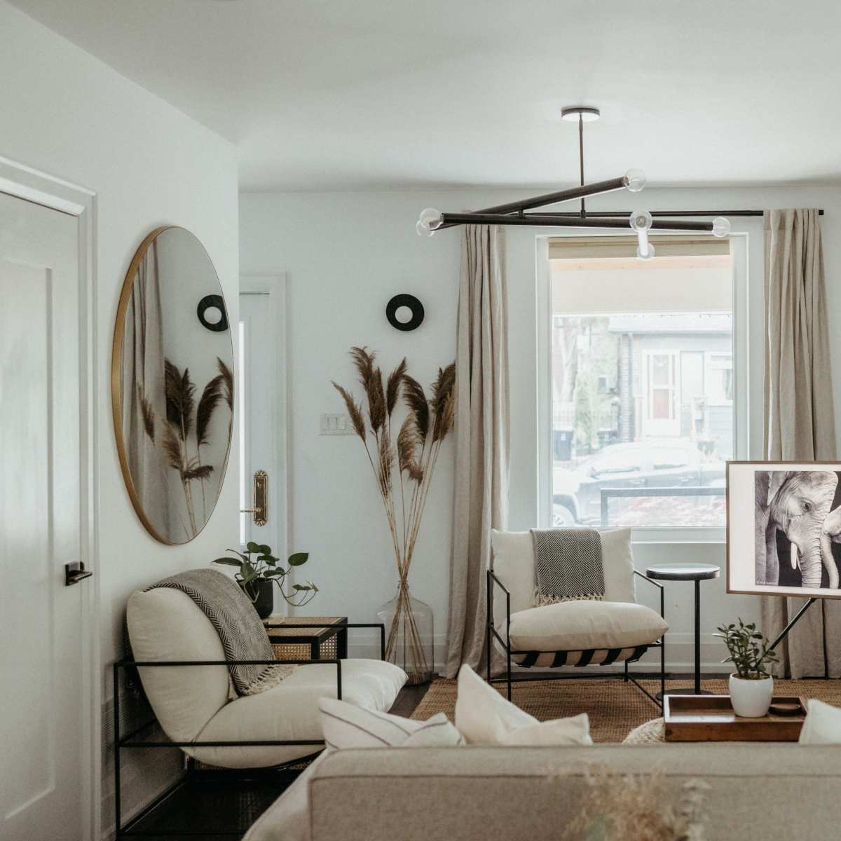 A modern living room featuring a light-colored sofa, a television displaying black-and-white artwork, and large windows with natural light.