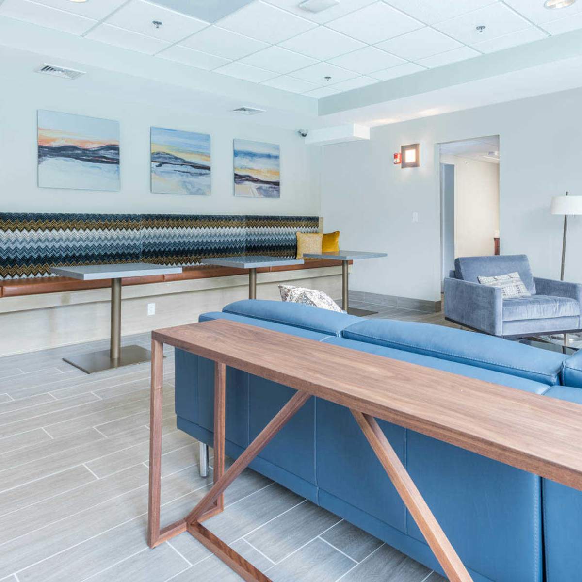 A modern lounge area with a blue sofa, a wooden table, an armchair, and abstract wall art.