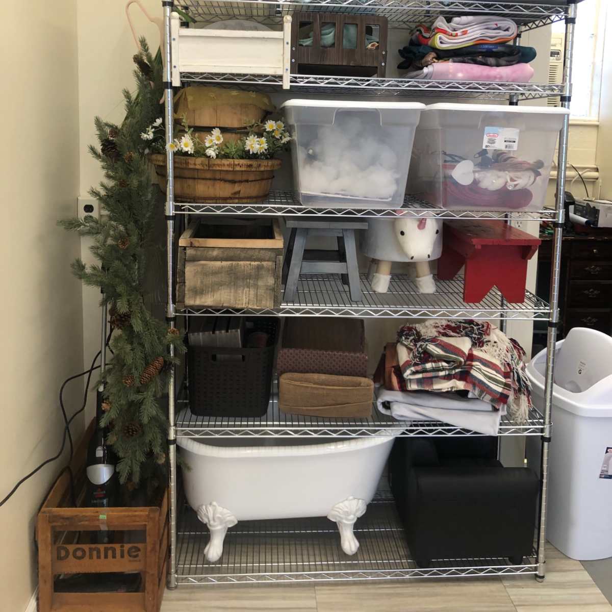 A metal shelving unit filled with various containers, baskets, and home decor items, alongside a small artificial Christmas tree.