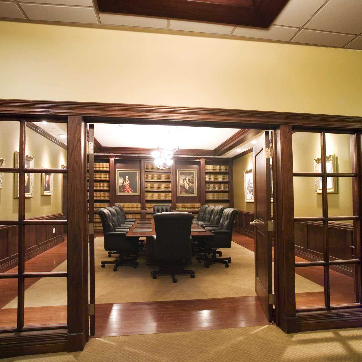 A well-furnished conference room with dark wood accents, a long table, and black chairs, framed by glass-paneled doors.