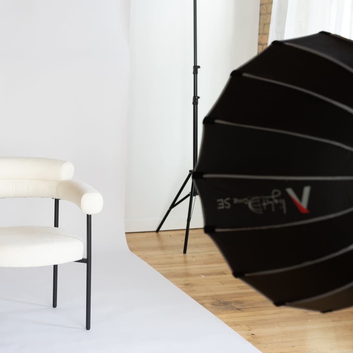 A white fabric chair with curved armrests is positioned in front of a plain backdrop in a photography studio.