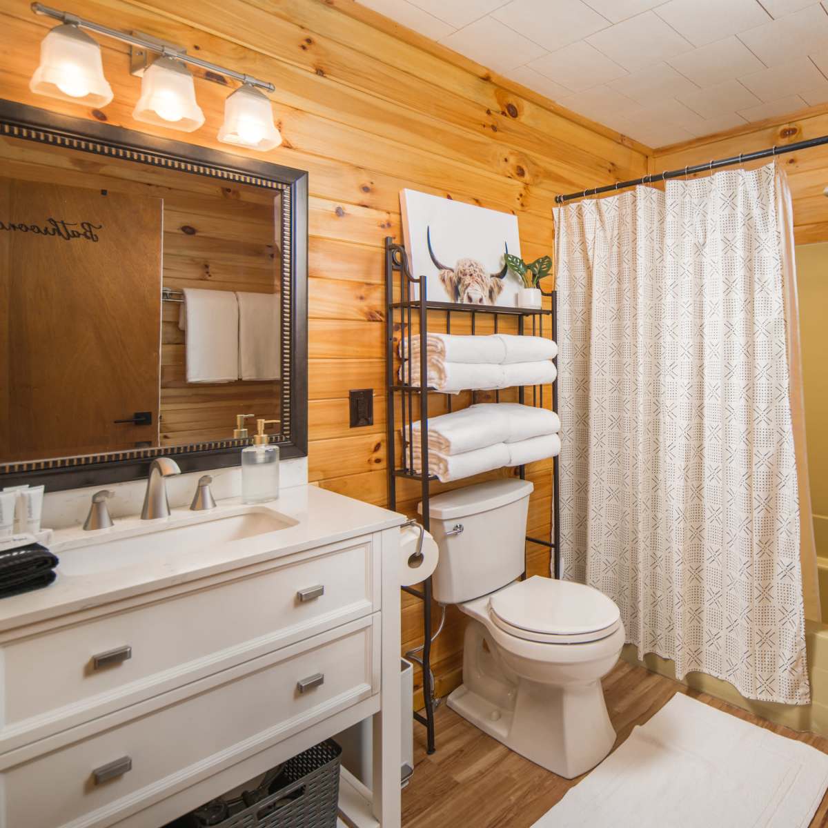 A wooden-paneled bathroom featuring a shower, toilet, sink with a mirror, and a stacked washer and dryer.