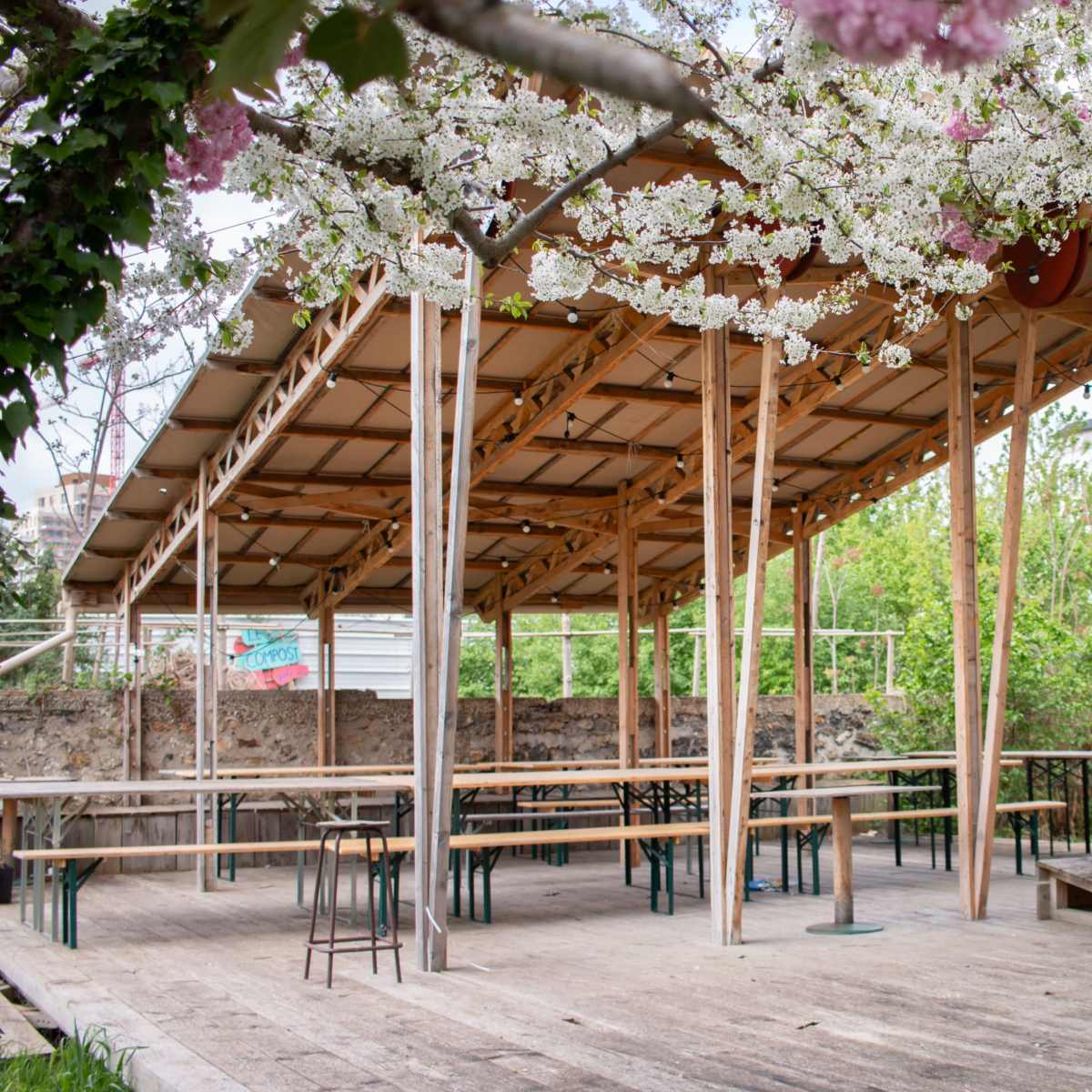 An outdoor pavilion with wooden beams and tables beneath flowering trees.