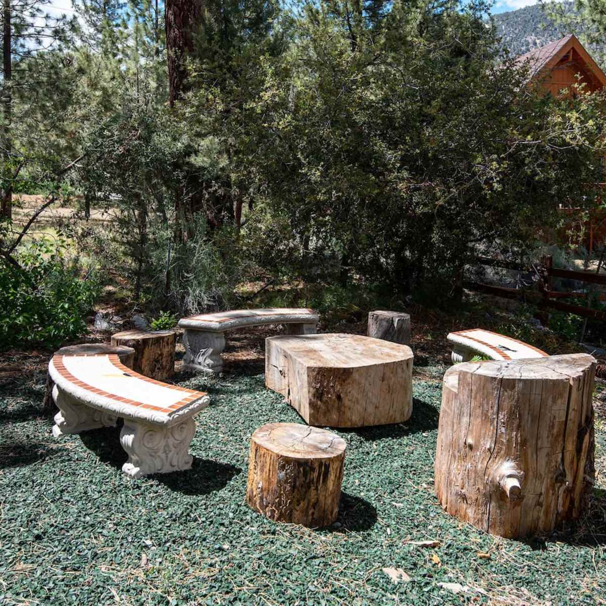 A rustic outdoor seating area made of sliced logs and stone benches, surrounded by greenery.